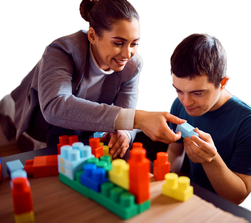 A cheerful woman and a young adult man are together at a table playing with brightly colored building blocks. The woman, with her hair pulled back, wears a gray sweater. She gestures towards the blocks as the man holds one in his hands, looking at it with a slight smile. This heartwarming photo is perfect for campaigns centered around learning, playing, and the support of others. The photo's bright, cheerful colors would also be great for educational materials or projects focused on childhood development and playful learning.